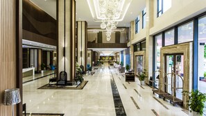 Un hall de hotel espacioso con techo alto, una lámpara central y un mostrador de recepción.