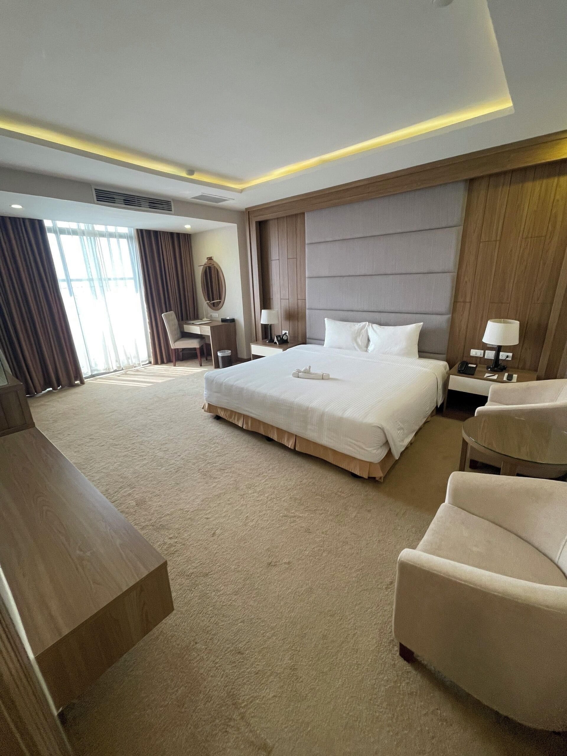 A modern hotel room with a large bed, a desk, a chair, and a sofa.