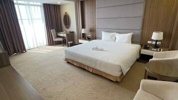 A modern hotel room with a large bed, a desk, a chair, and a sofa.