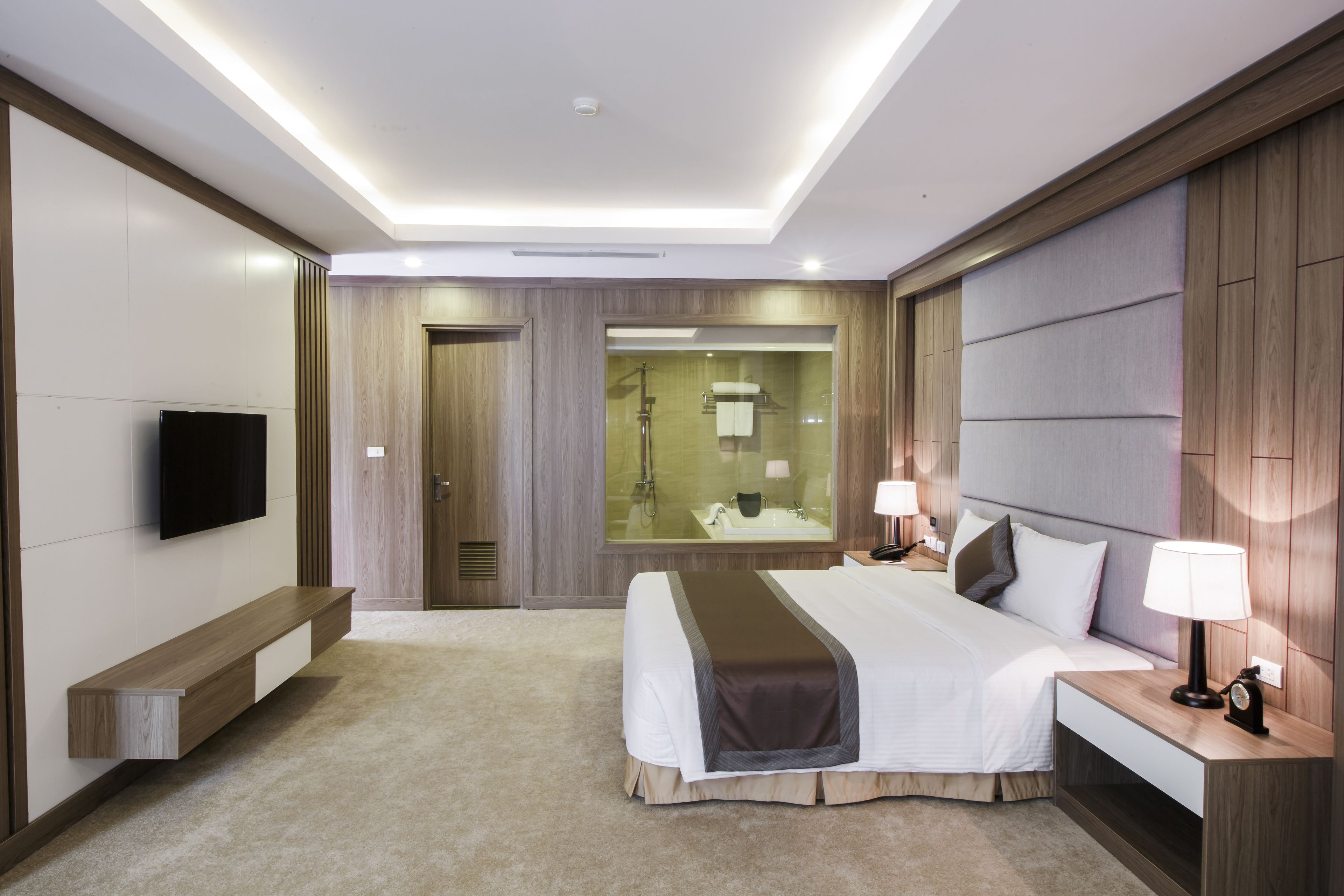 A modern hotel room with a large bed, bedside lamps, a TV, and a bathroom with a mirror and shower.