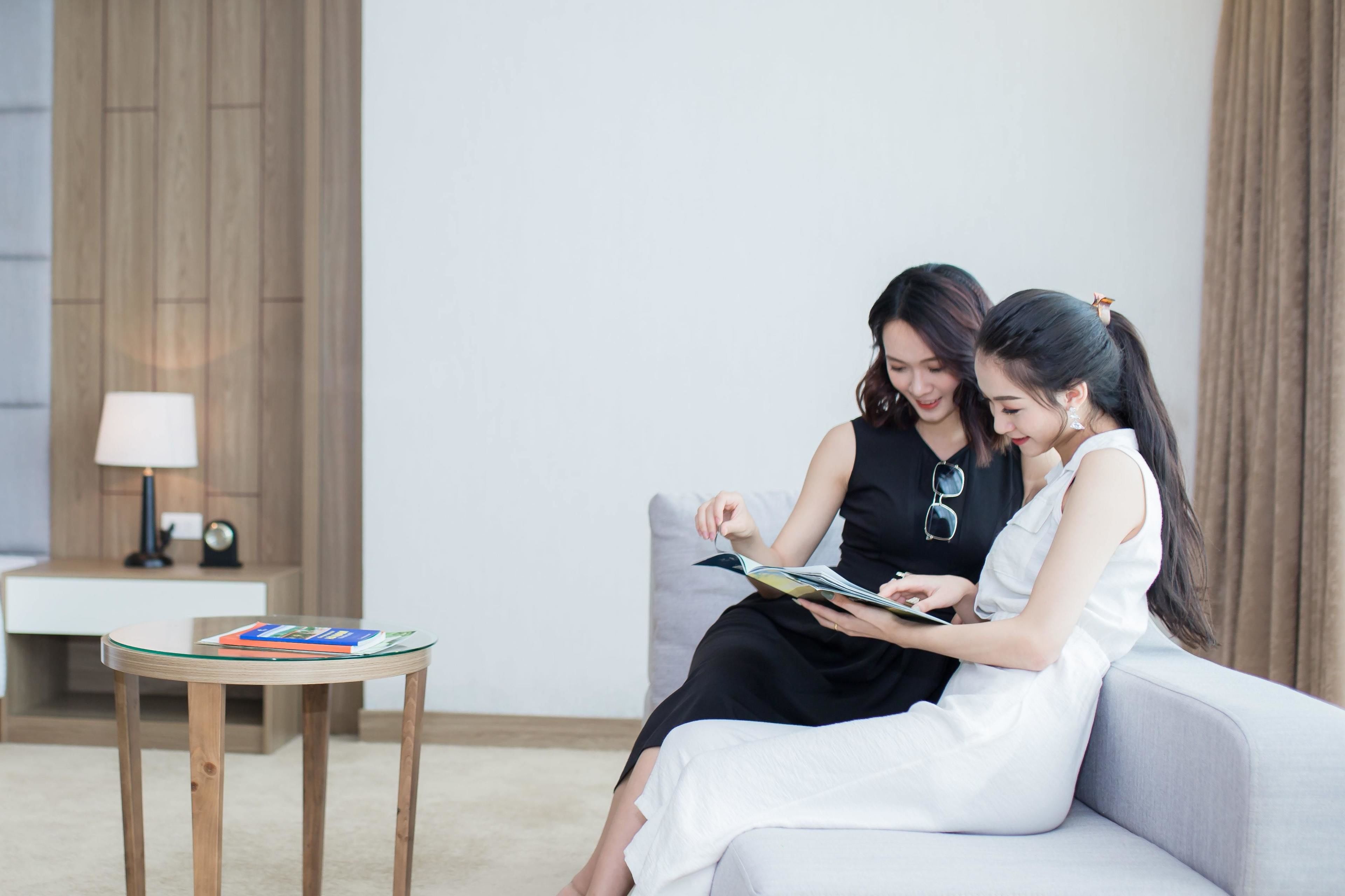 Two people sitting on a grey sofa, reading a magazine. A small wooden table with a glass top is in front of them, holding a magazine.