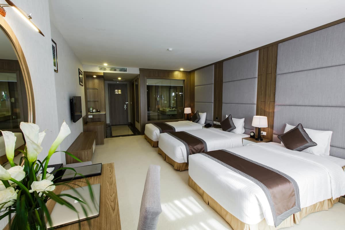 Habitación de hotel con dos camas, un escritorio, una silla, un espejo y un florero con flores.