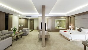 A modern hotel room with a sofa, a coffee table, a bed with a white duvet, and a large mirror.
