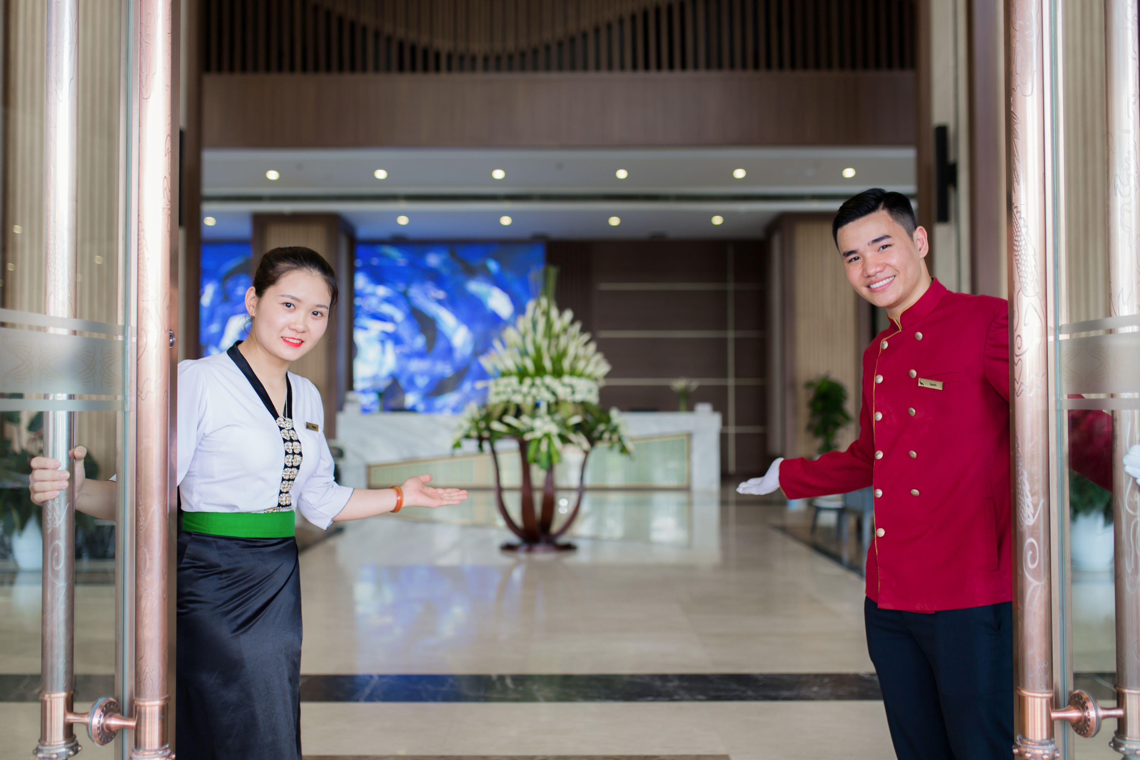 Een hotel lobby met een receptiebalie, een groot scherm en een decoratieve plant.