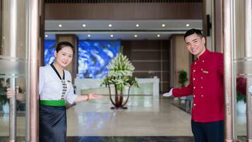 Een hotel lobby met een receptiebalie, een groot scherm en een decoratieve plant.