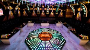 A bar area with a central circular platform, multiple seating areas, and a ceiling adorned with hanging lights.