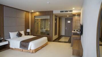 A modern hotel room with a large bed, a bedside table, a mirror, a shower area, and a small desk with a chair.
