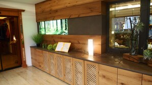 Ein Empfangsschalter mit Holzpaneelen, ein großes Fenster mit Blick auf einen Wald und eine Vitrine mit Pflanzen.