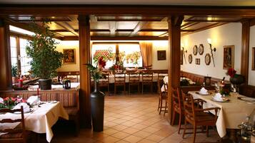 A dining area with multiple tables and benches, a large vase with flowers, and a window with curtains.