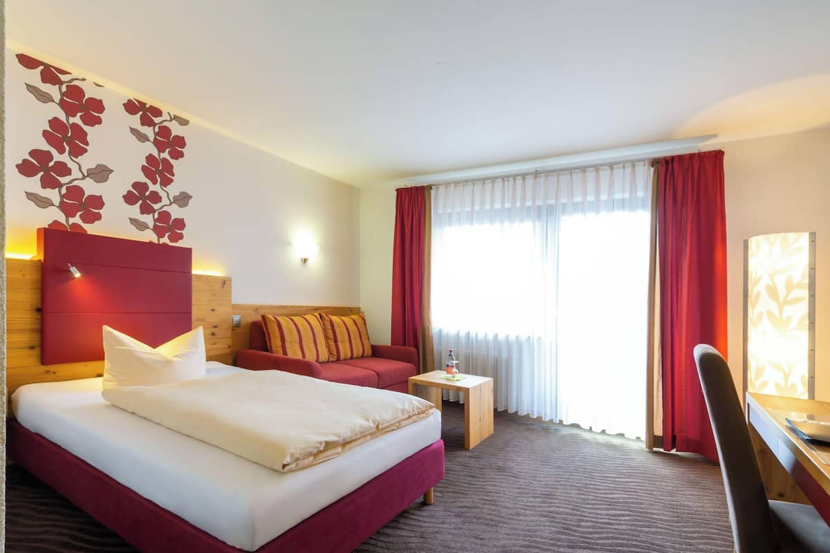 Ein Hotelzimmer mit einem Bett, einem Schreibtisch, einem Stuhl, einem kleinen Tisch und einem Fenster mit Vorhängen.