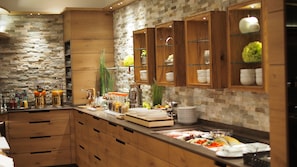 A modern kitchen with wooden cabinets, a stone backsplash, and a variety of food items and beverages on the counter. - Hotel Restaurant Bierhäusle (Freiburg im Breisgau)