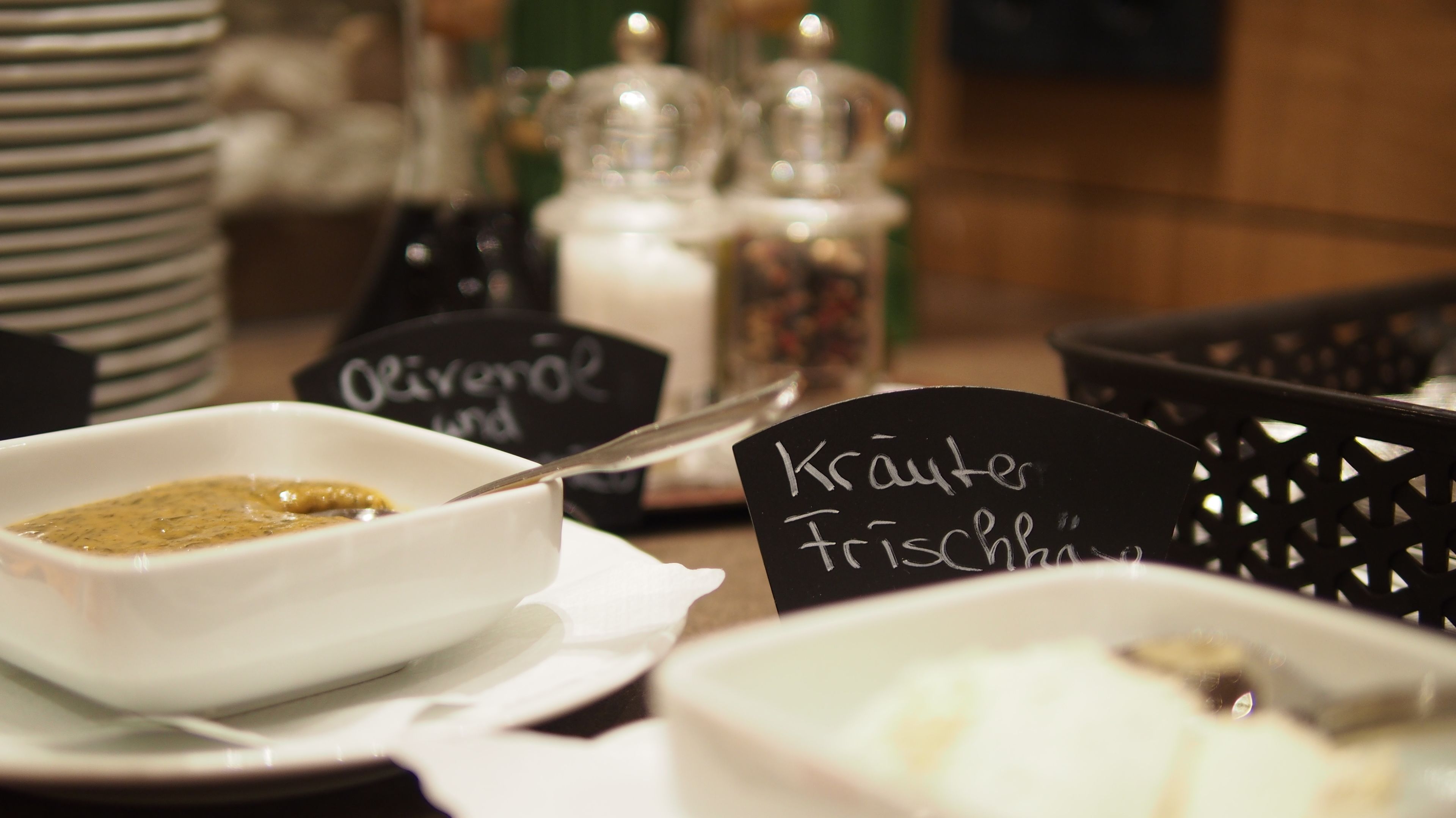 Una mesa con un tazón blanco que contiene una salsa verde, un letrero negro con la inscripción 'Kräuter Trödel' y una cuchara dentro del tazón.