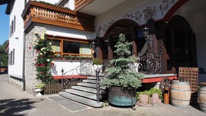 Ein traditionelles Gebäude mit einem hölzernen Balkon, einer Steintreppe und einem kleinen Baum im Vordergrund.