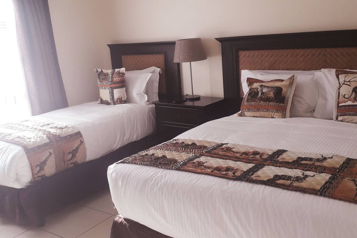 A hotel room with two single beds, a nightstand with a lamp, and a window with curtains.