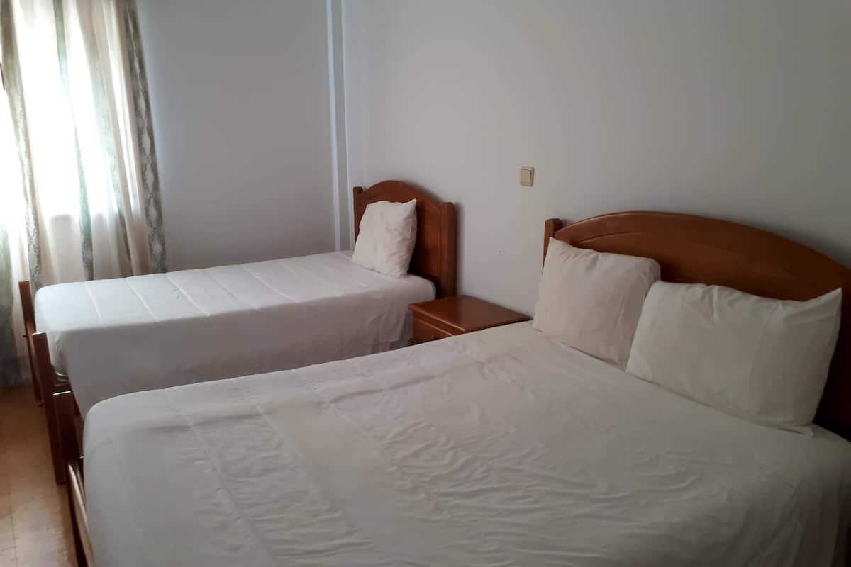 A hotel room with two single beds, wooden headboards, white bedding, and a nightstand with a lamp.