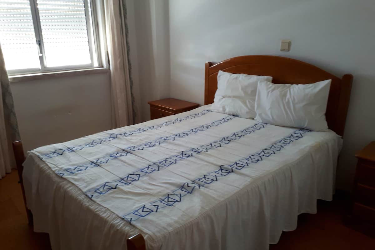 A single bed with a white and blue patterned bedspread, a wooden headboard, and a nightstand with a lamp.