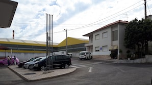 A parking area with several cars, a pedestrian crossing, and buildings with signage. - Mira Tejo (Loures)