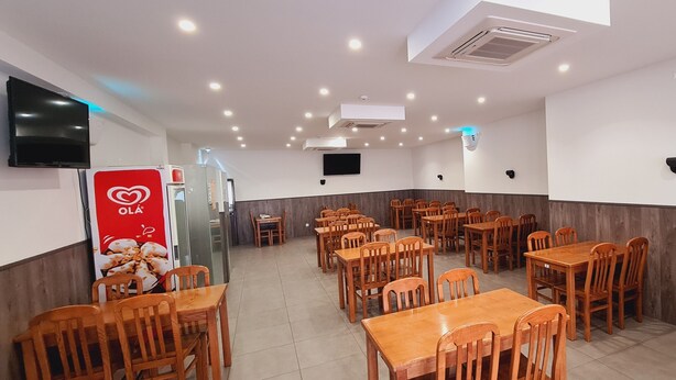 A restaurant with multiple wooden tables and chairs, a TV mounted on the wall, and a sign with a heart symbol. - Mira Tejo (Loures)