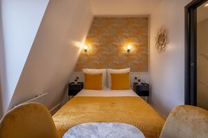 Quarto pequeno e moderno com cama, duas mesas de cabeceira e um criado-mudo.