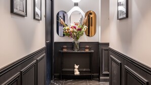 A hallway with a black console table, a vase with flowers, and a white cat statue. - Mijo's Appartements Hôtel (Fontenay-sous-Bois)