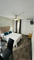 Habitación de hotel con cama, escritorio, silla, ventilador de techo, televisor y armario.