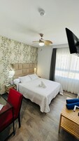 Een hotelkamer met een bed, een bureau, een stoel, een plafondventilator en een aan de muur bevestigde televisie.