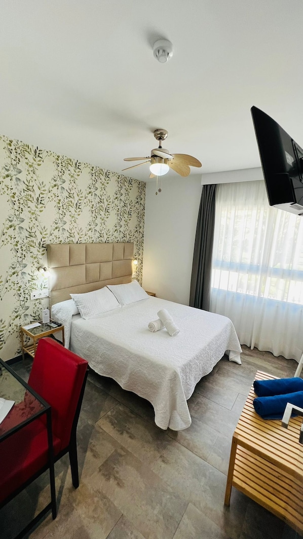 A hotel room with a bed, a desk, a chair, a ceiling fan, and a TV mounted on the wall. - Bajondillo Beach Cozy Inns (Torremolinos)