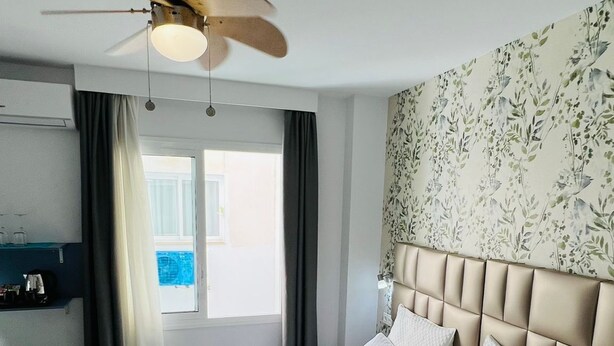 A hotel room with a bed, a ceiling fan, a window with curtains, and a wall with floral wallpaper. - Bajondillo Beach Cozy Inns (Torremolinos)