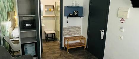 Quarto de hotel com cama, escrivaninha, cadeira, armário, ventoinha no teto e porta.