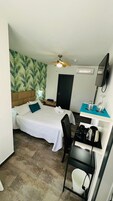 Een hotelkamer met een bed, een bureau met een waterkoker, een stoel, een televisie en een deur.