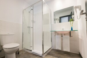 Een moderne badkamer met een douchecabine van glas, een wit toilet, een wastafel met een glazen blad en een spiegel boven de wastafel.