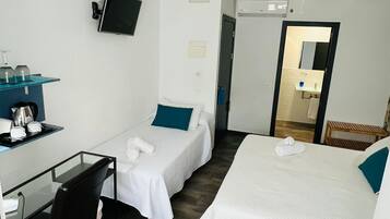 Een hotelkamer met twee bedden, een bureau met stoel, een televisie en een plafondventilator.