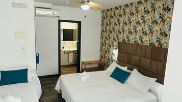 Une chambre d’hôtel avec deux lits, un bureau et une salle de bain visible à travers une porte ouverte.