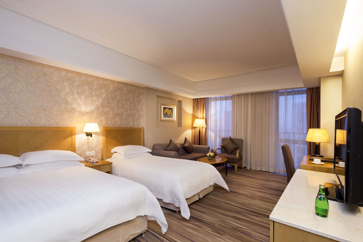 A hotel room with two beds, a sofa, a desk, and a TV.