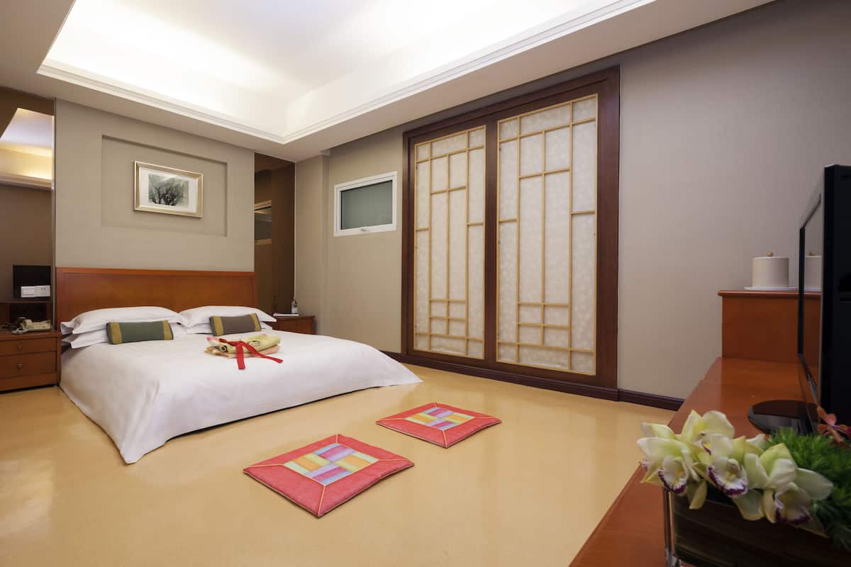 A hotel room with a bed, bedside tables, a TV, a sliding door, and a small desk with a lamp.