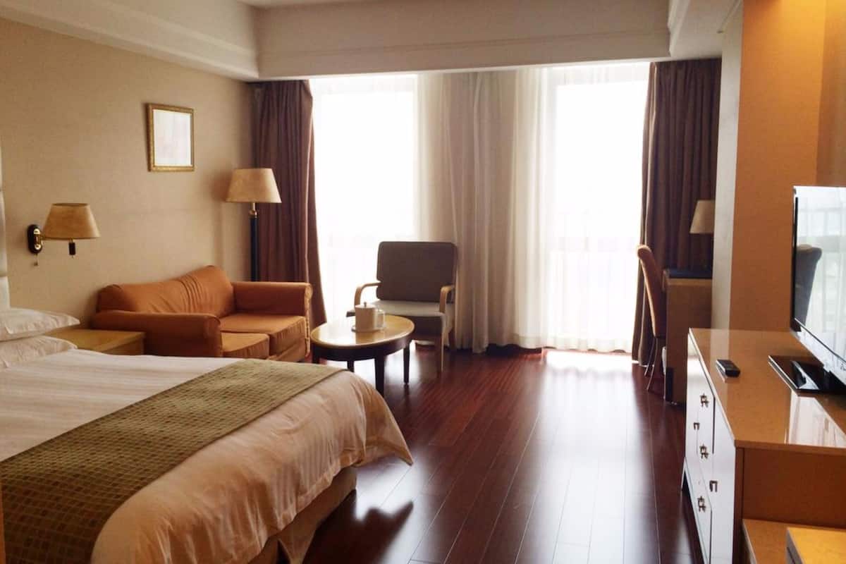 A hotel room with a large bed, a sofa, a chair, a small table, a TV, and a window with curtains.