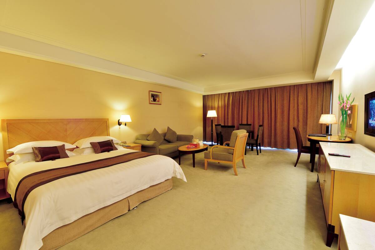 A hotel room with a large bed, a sofa, a desk, and a chair.