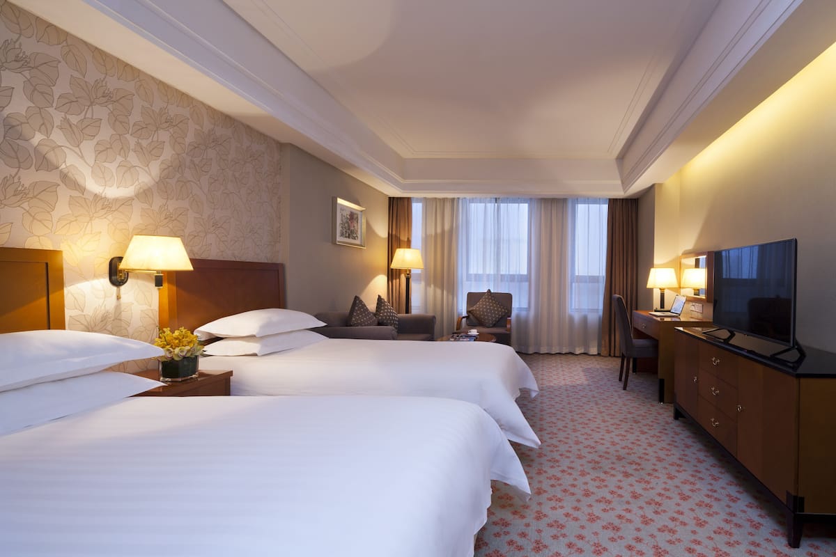 A hotel room with two beds, a desk, a television, and a view of the outdoors.