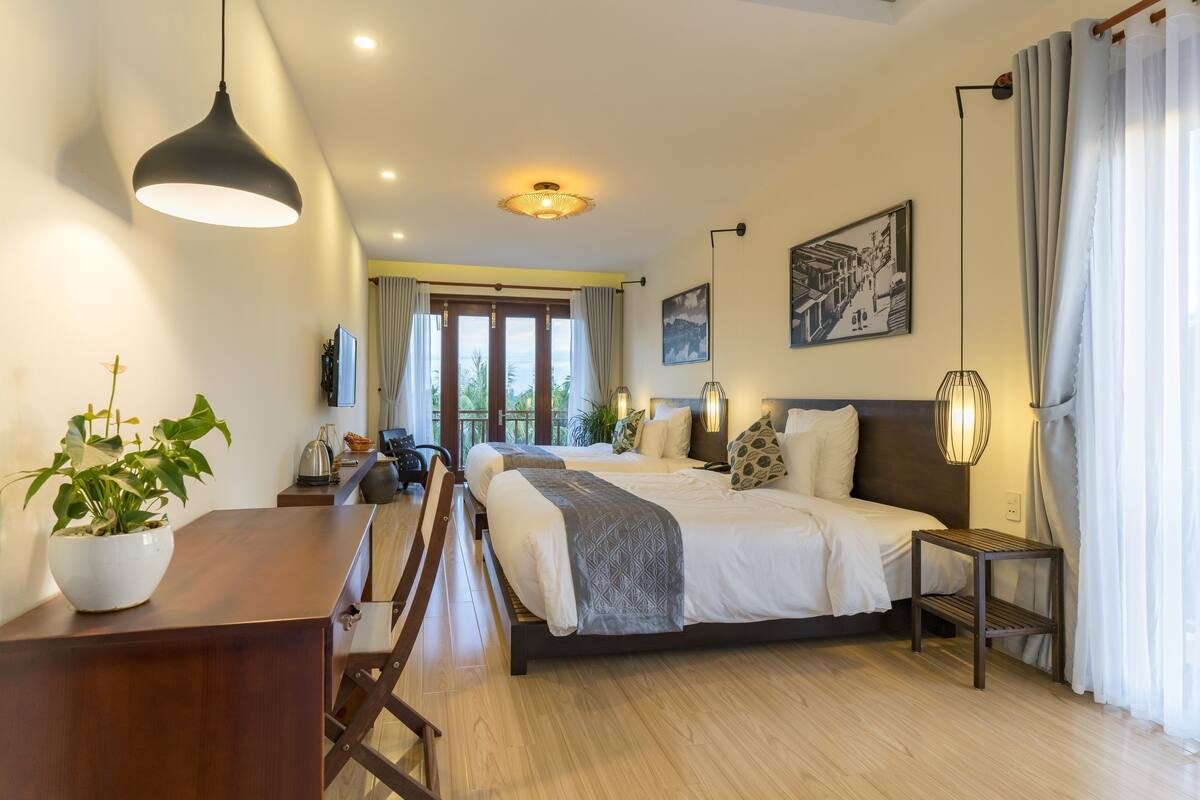 A modern hotel room with a large bed, a desk, a chair, and a potted plant.
