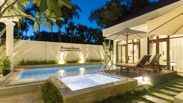 Une piscine entourée d’une terrasse en pierre, de chaises longues et d’un espace salon couvert agrémenté de parasols.