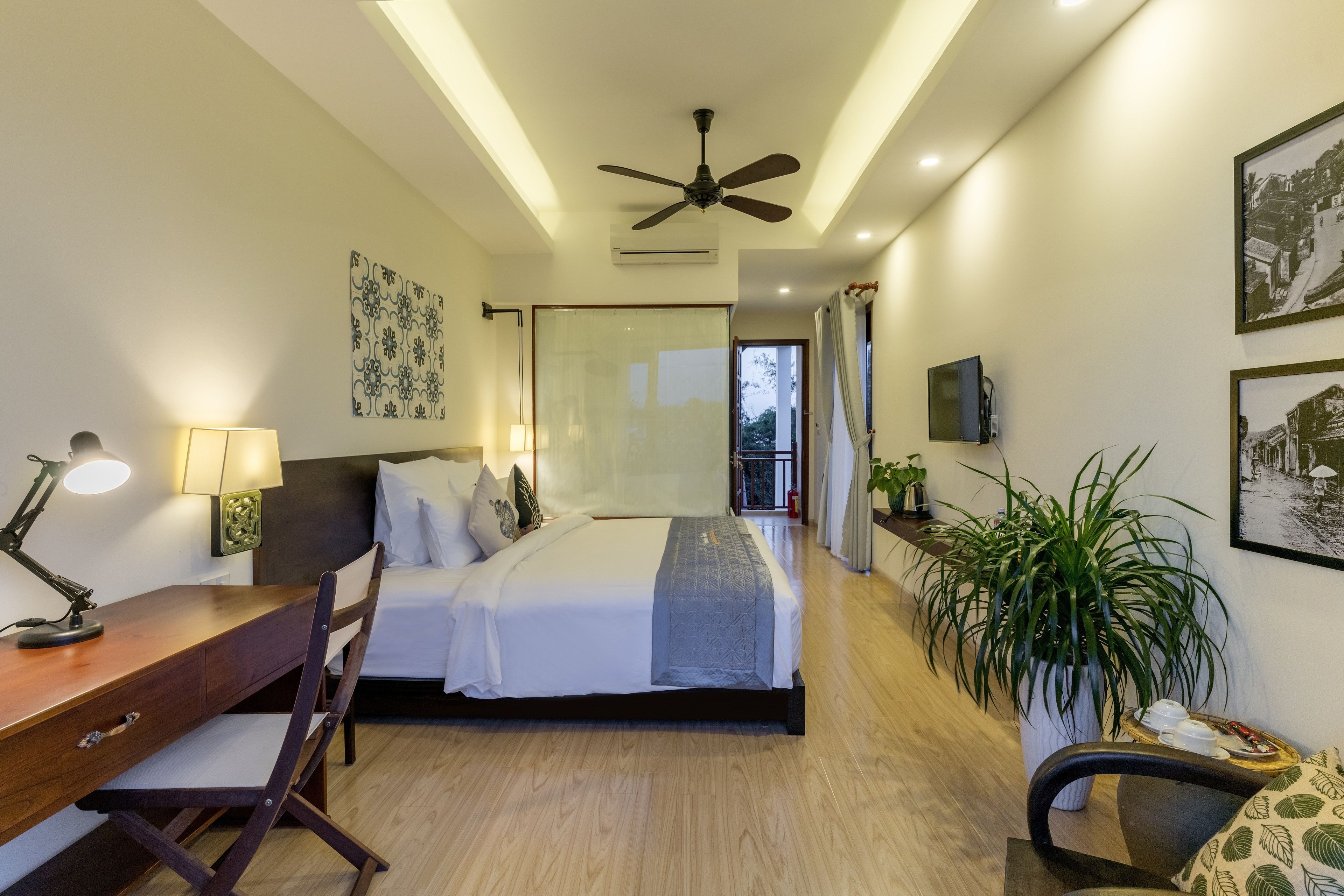 A modern hotel room with a bed, desk, chair, and potted plants.