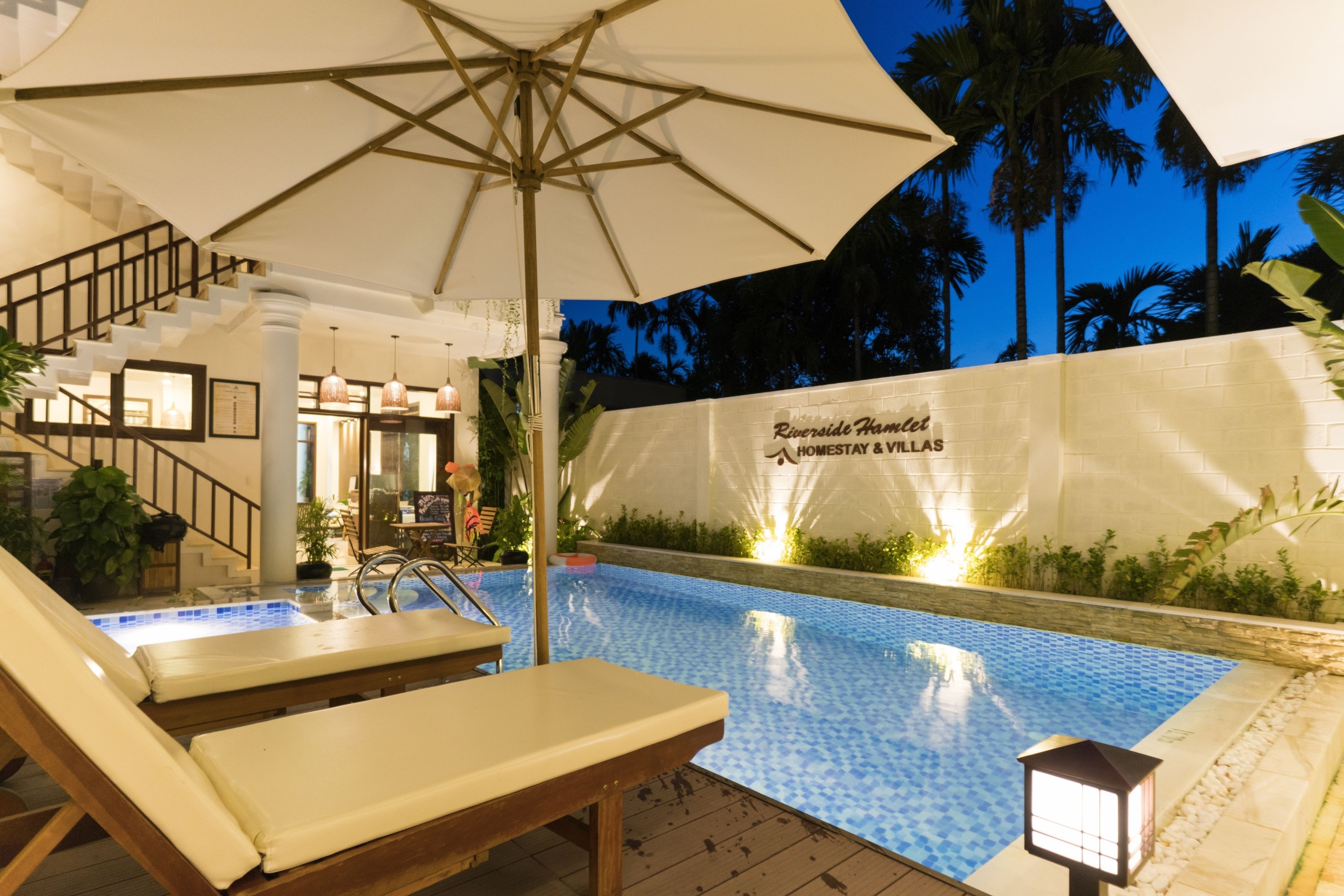 A pool area with lounge chairs and umbrellas, a staircase, and a wall with the text "Riverside Hotel".