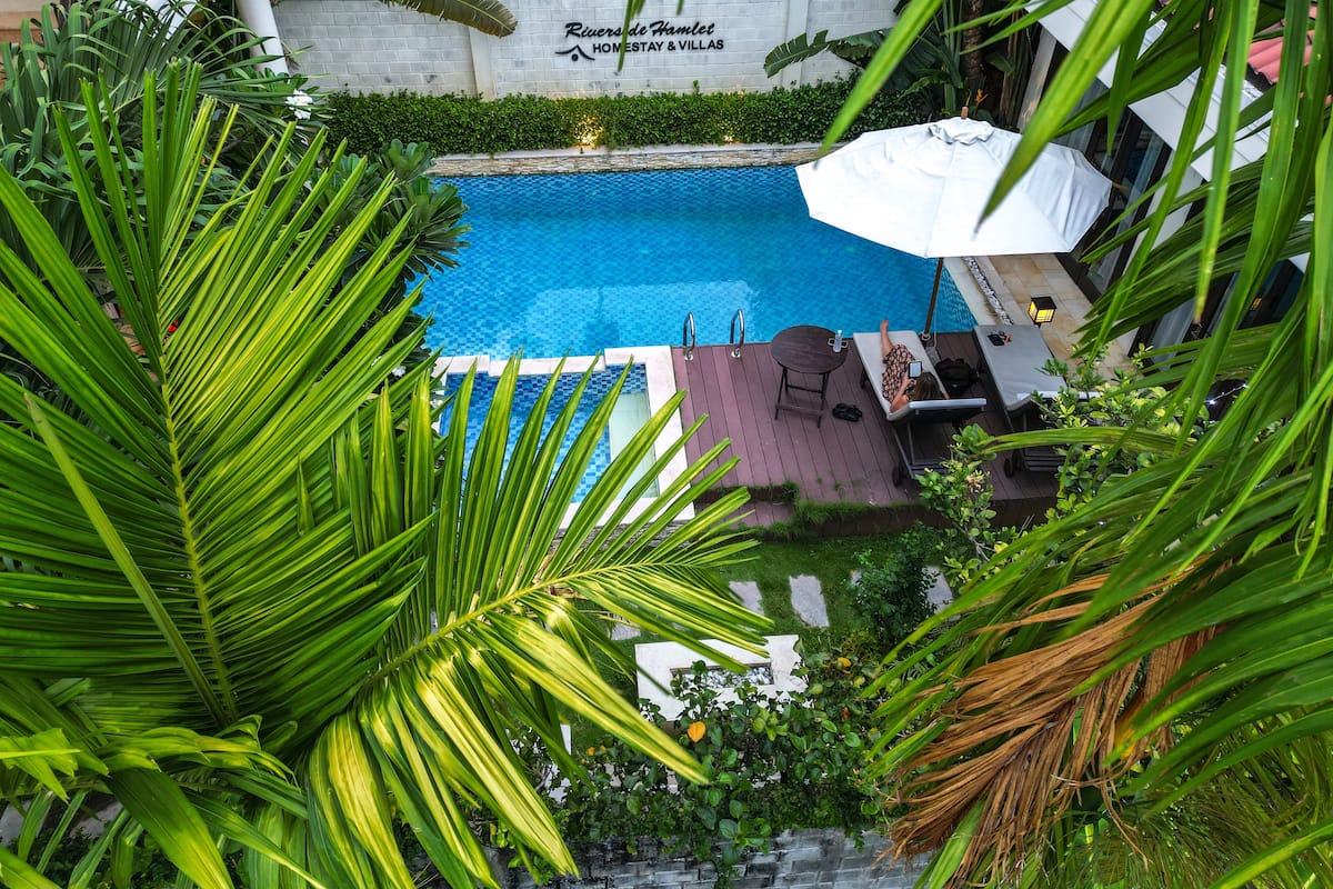 A swimming pool with a view of a building labeled "Rivers de Hamlet Homestay & Villas".