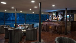 A bar area with wicker furniture and a view of a rocky coastline. - Orchid Trendy Cruise (Tuan Chau)