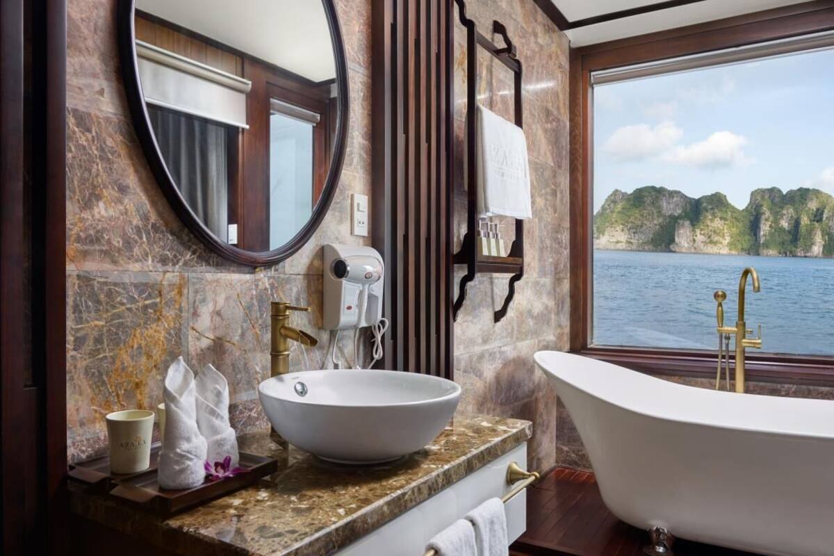 A bathroom with a large oval mirror, a white vessel sink, a freestanding bathtub, and a view of a body of water.