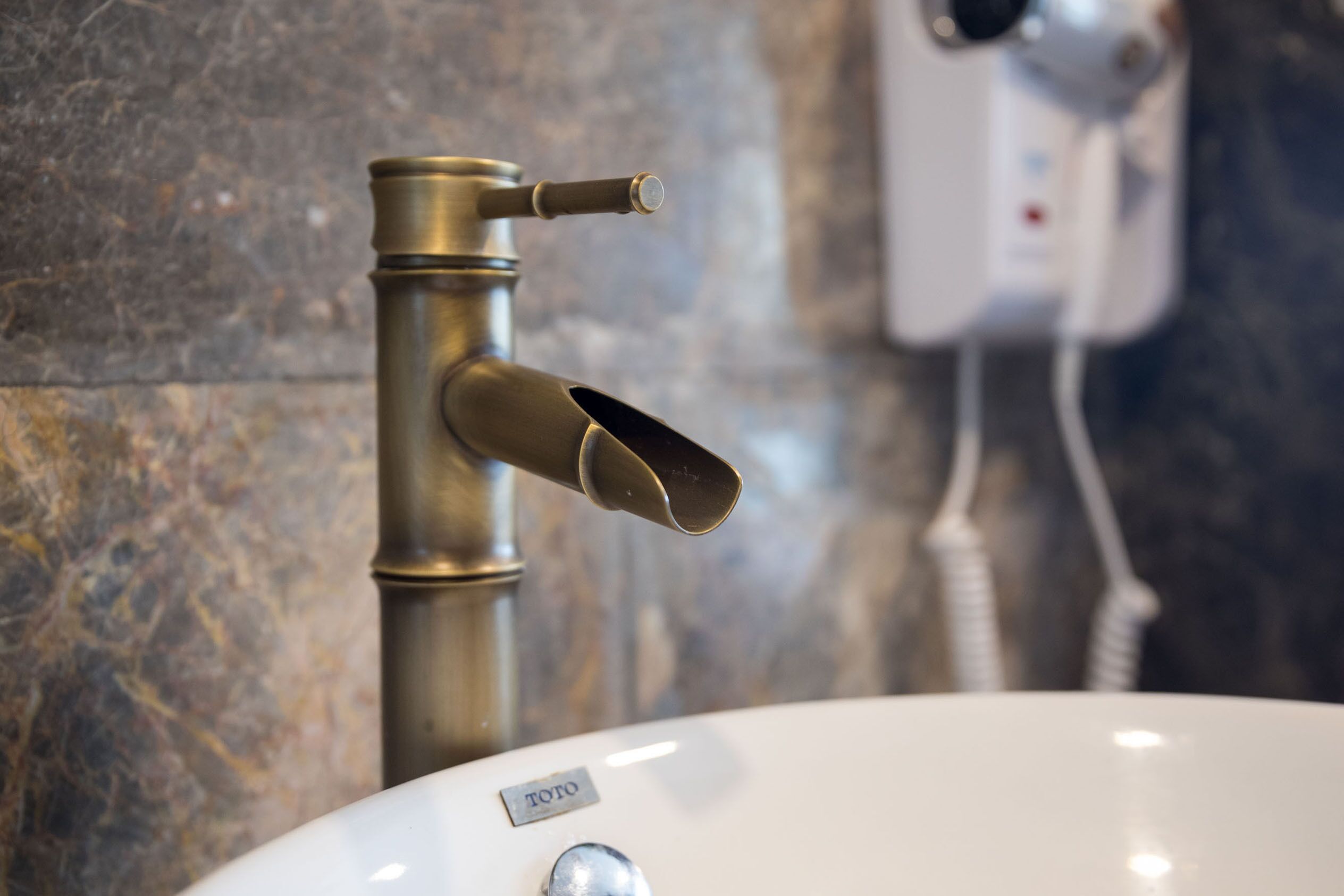 A bathroom sink with a brass faucet and a hairdryer mounted on the wall.
