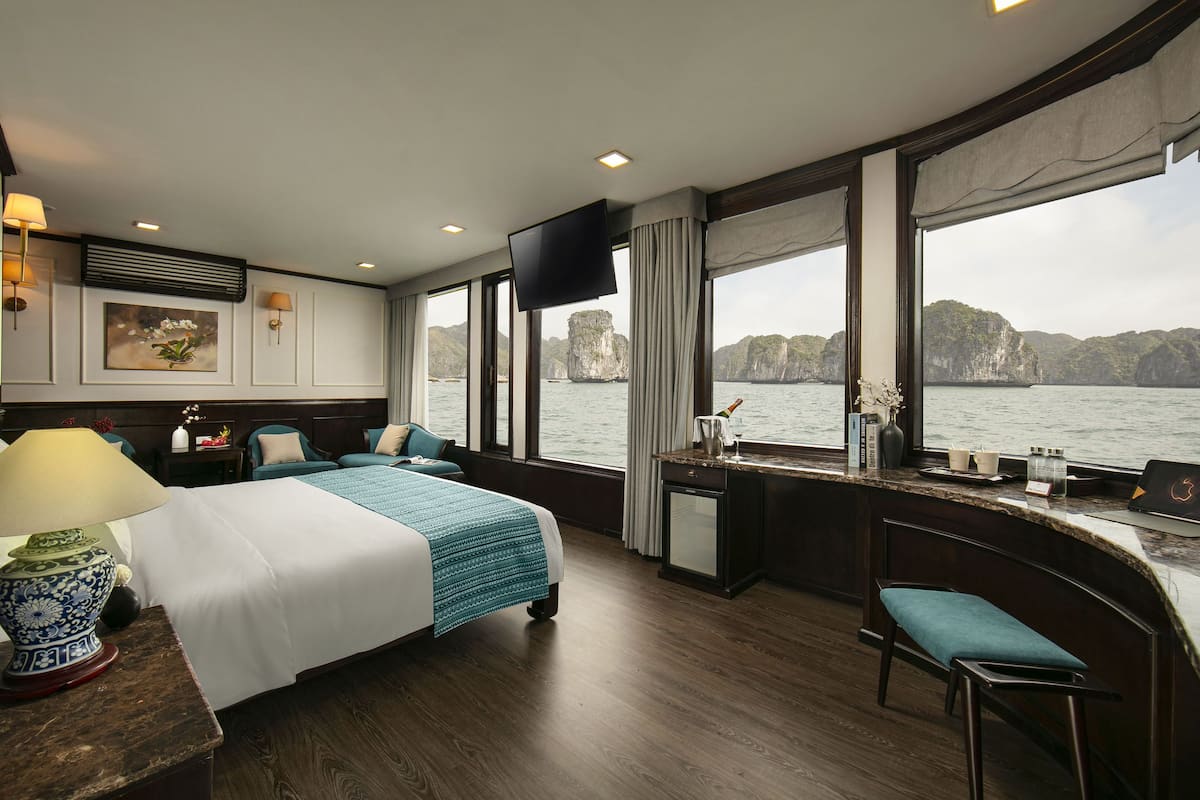 A modern hotel room with a large bed, a desk, and a view of the sea.