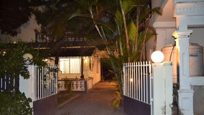 Une entrée fermée par un portail mène à un bâtiment, et un chemin y conduit jusqu’à une pièce éclairée.