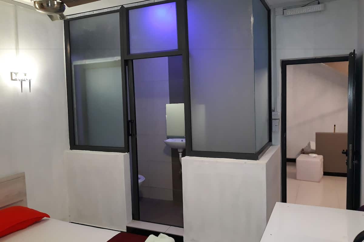 A room with a bed, a red pillow, a white table, and a window with frosted glass panels.