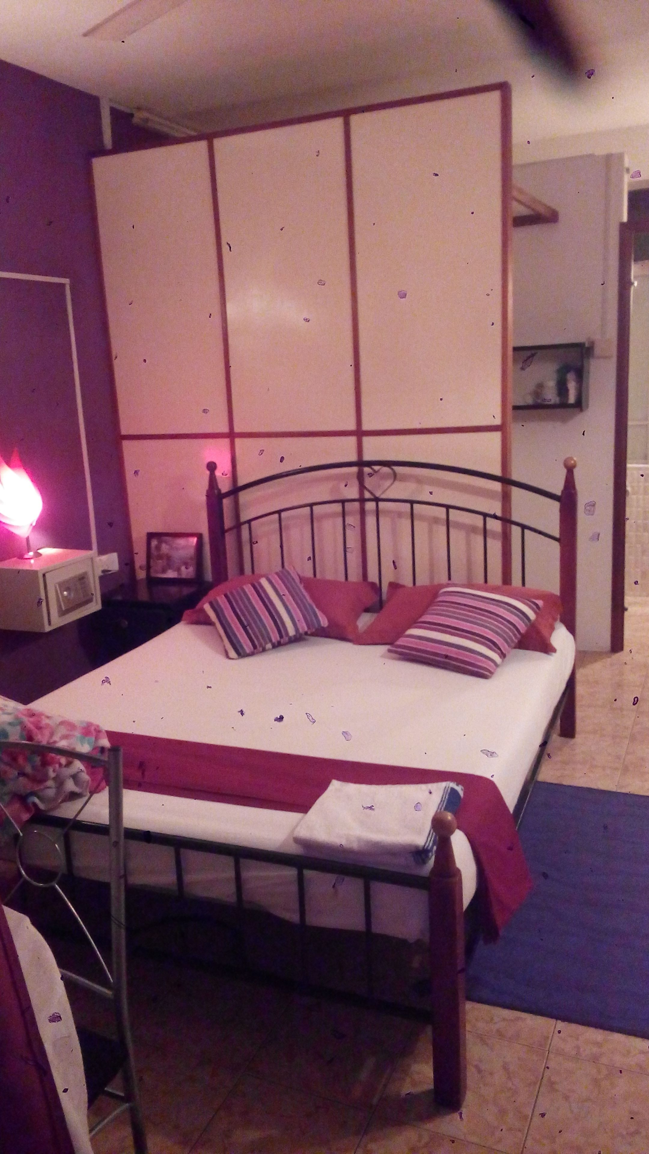 Un lit simple avec un cadre en métal, une table de chevet avec une lampe et une petite chaise.